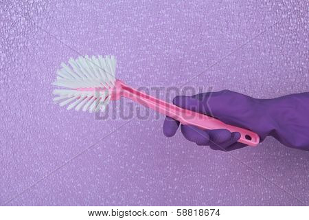 Toilet brush in hand on purple background
