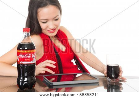 NAKHODKA, RUSSIA - JANUARY 18, 2014: Girl holding a glass of Coca-Cola on the table is a bottle of Coca-Cola. Coca-Cola is a very popular carbonated soft drink sold in shops, restaurants worldwide.   