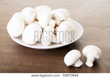 Fresh raw mashroom lying on a plate. Over wooden background.