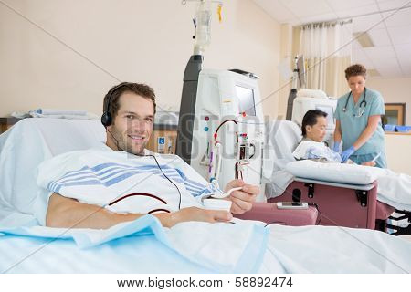 Portrait of young male dialysis patient holding glass of crushed ice during renal dialysis at hospital
