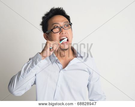 Asian business man woke up late, brushing teeth in hurry, on plain background