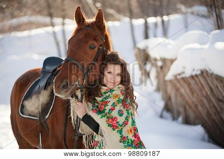 beautiful young woman in Russian national scarf with a horse in the countryside in winter