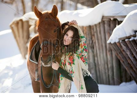 beautiful young woman in Russian national scarf with a horse in the countryside in winter