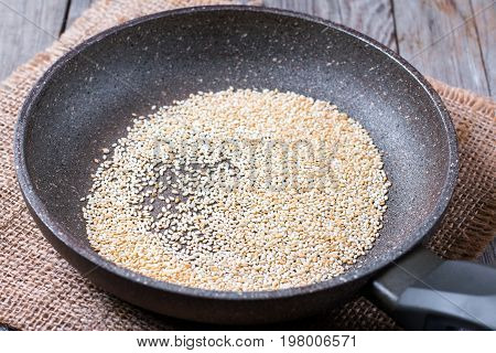 Sesame seeds are fried in the pan on a wooden table