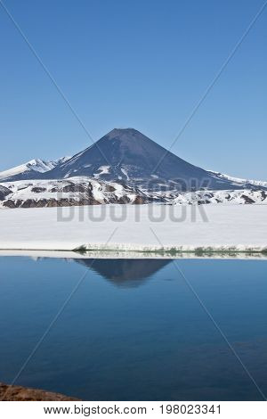 Look at Karymsky volcano from the hot springs and geyser Karymsky lake in spring in Kamchatka Russia snow may reflection