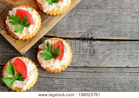Home mini sandwiches with cream cheese on a wood background with empty place for text. Quick mini sandwiches from crackers cookies, spicy cream cheese, tomato and parsley. Tasty snack recipe. Top view