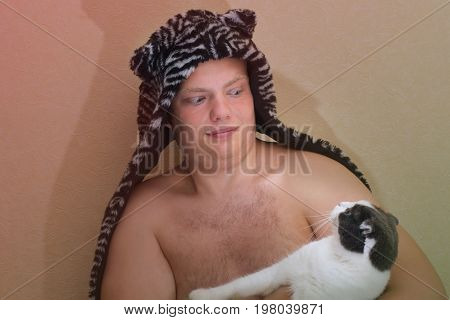 The boy in a hat is holding a cat they looking at each other with surprise