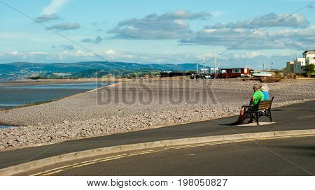 Minehead UK - July 27 2016: Mature couple in love relaxing in a beach of Minehead UK enjoying ocean view together sitting in a bench
