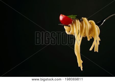 Spaghetti on a fork spaghetti with cherry tomato and fresh basil isolated on black background with copy space. Healthy and vegetarian food concept.