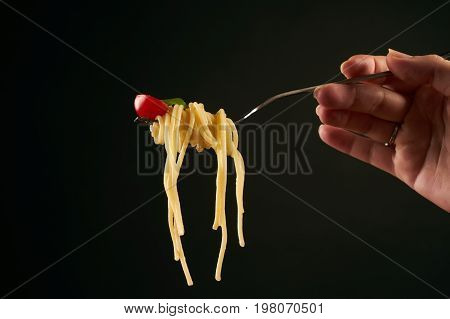 Closeup of a spaghetti on a fork. Girl keeping fork with spaghetti. Pasta with red sauce and tomato isolated on black background with copy space. Healthy vegetarian food