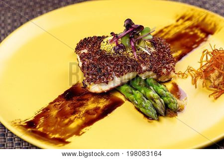 Quinoa crusted fish on asparagus on yellow plate on Wicker place mat