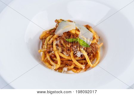 Pasta with tomato sauce and parmesan in white plate on white tablecloth.