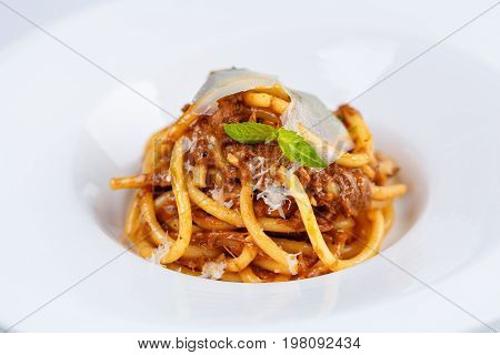 Pasta with tomato sauce and parmesan in white plate on white tablecloth.