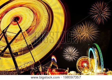 colorful ferris wheels and carnival rides in motion at night with fireworks in the sky