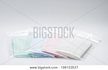 Green pink light blue and white ear loop disposable face mask in plastic bag overlapping used for covering mouth and nose. It protects against body fluid and large particles in the air