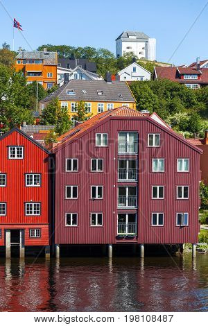 Famous wooden colored houses in Trondheim city Norway. Colorful houses on stilts and flag of Norway in sunny day.