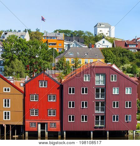 Famous wooden colored houses in Trondheim city Norway. Colorful houses on stilts and flag of Norway in sunny day.