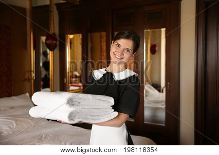 Chambermaid holding clean towels in hotel room