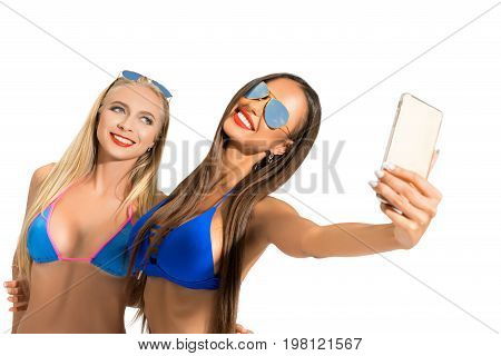 Sexy girls wearing sunglasses and blue bicinis posing in studio making selfie