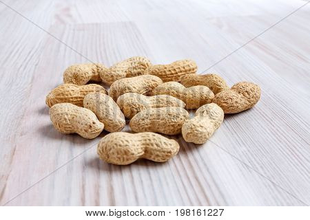 A heap of unpeeled peanuts on a light kitchen table close-up.