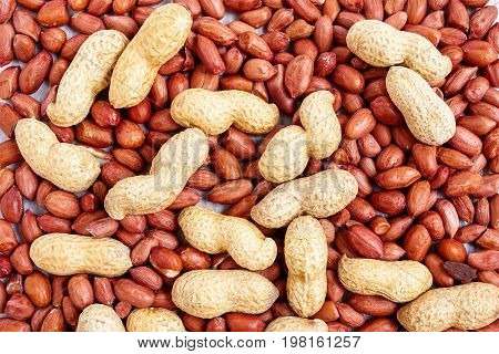 A heap of unpeeled and peeled peanuts close-up for use as background.