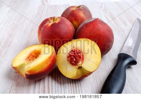 A few ripe juicy peaches on a light table. One peach is cut into two halves.