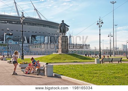 SAINT - PETERSBURG, RUSSIA - AUGUST 1, 2017: People on The Krestovsky Island near Sergei Kirov Statue. On the background is Krestovsky Stadium (Zenit Arena) by Kisho Kurokawa architect