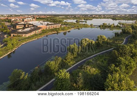 Aerial view of a lake beside a community center with walking paths and bridge in The Glen, Glenview, Illinois.