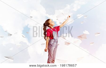 Little cute girl against sky background playing with paper airplane