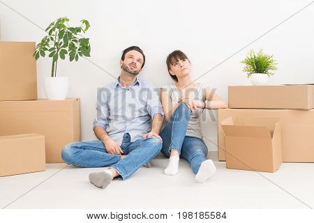 A young couple sitting on the floor and looking up. Dream and enjoy your new home.