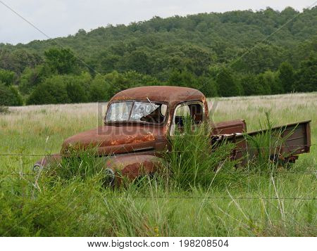 Rusty old pickup truck with shattered windshield parked in a grassy patch, with a for sale sign