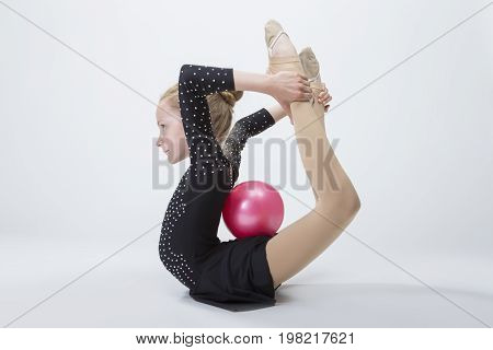 Sport Concepts. Caucasian Female Rhythmic Gymnast In Professional Competitive Black Sparkling Suit Doing Backbend Stretching Exercise With Ball in Studio On White. Horizontal Image