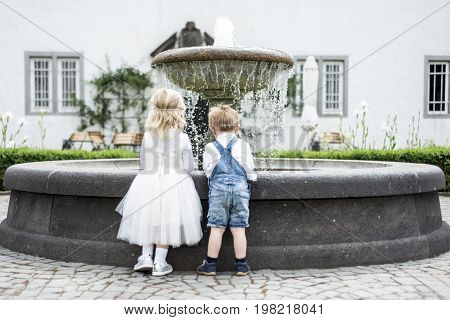 backview Little girl and boy in wedding dress with old classic style stone fountain with flowing water concept sewwt love romantic be togehther couple
