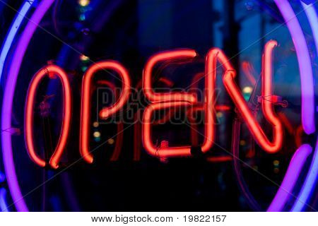 Insegna al neon blu, viola e rosso della parola 'Open' all'interno di due anelli, di illuminazione, su uno sfondo nero