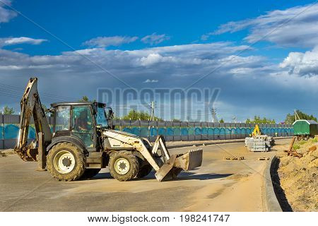 Tractor with bucket performs excavation work. Construction of high-speed bypass road around Krasnoe Selo Saint Petersburg. Heavy machine equipment for excavation works industrial construction. Russia