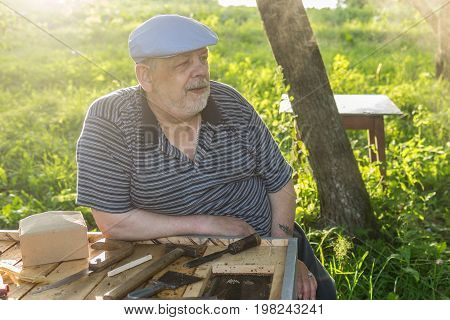 Outdoor portrait of elderly bee-keeper sitting near beehive