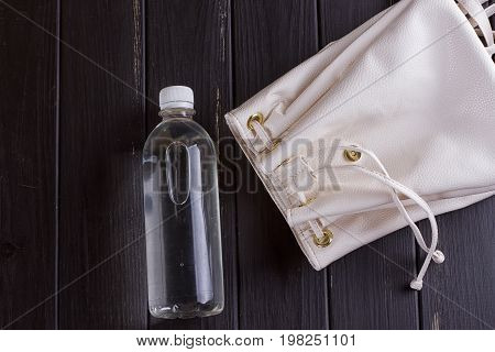 White leather backpack and water bottle on a black wooden background