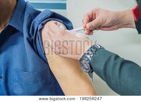 Close up of patient getting a vaccination in the hospital. The injection are treated by a nurse on the patient's upper arm with sterile equipment.