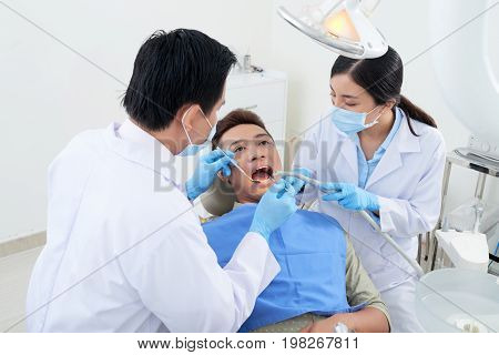 Dentist and nurse using mouth mirror, suction tube and dental explorer when examining teeth of patient