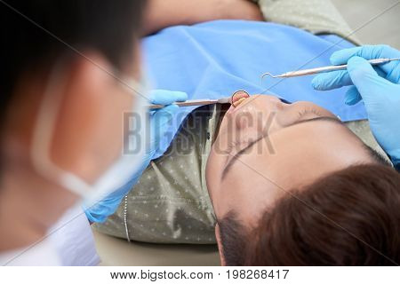 Close-up image of dentist examining teeth with dental explorer and mouth mirror