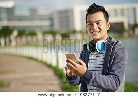 Happpy Vietnamese young man choosing track on his smartphone to listen to