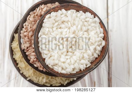 Set various organic raw rice on a wooden white table in ceramic bowls. Devzira. Arborio. Selective focus
