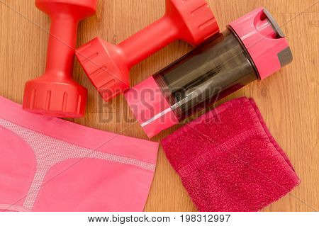 Athlete's set with female clothing, pink dumbbells and bottle of water on wooden background.