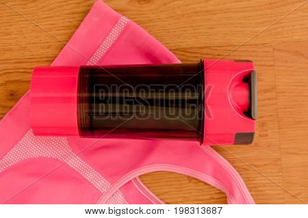 Athlete's set with a bottle of water over a pink sport bra on wooden background.