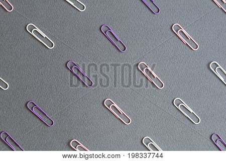 Top view on the pattrn of colored paper clips on the gray paper. Office work concept.