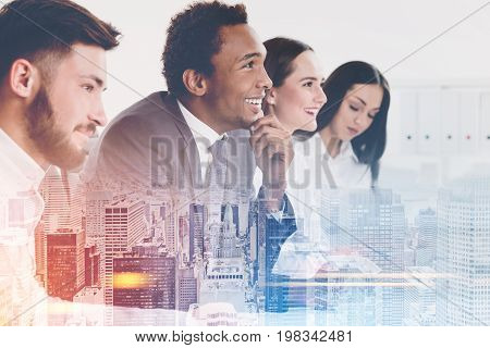 Side view of members of a business team sitting together at a table and looking at a person off camera and listening to them. Cityscape. Mock up toned image double exposure