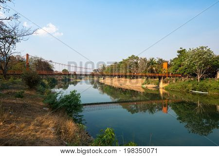 Horizontal picture of orange bridge over the Nam Song River with tropical vegetation. Close to Tham Chang Cave in the city of Vang Vieng Laos.