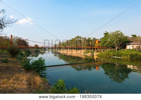 Wide angle picture of orange bridge over the Nam Song River with tropical vegetation. Close to Tham Chang Cave in the city of Vang Vieng Laos.