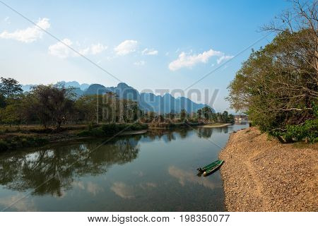 Beautiful sunny day of the Nam Song River with tropical vegetation and two boats. Close to Tham Chang Cave in the city of Vang Vieng Laos.