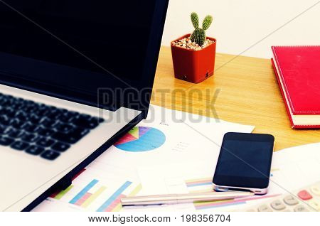 close up business accessories laptop calculator datasheet pen notebook and smartphone on desk financial report saving and economy business concept selective focus vintage color tone